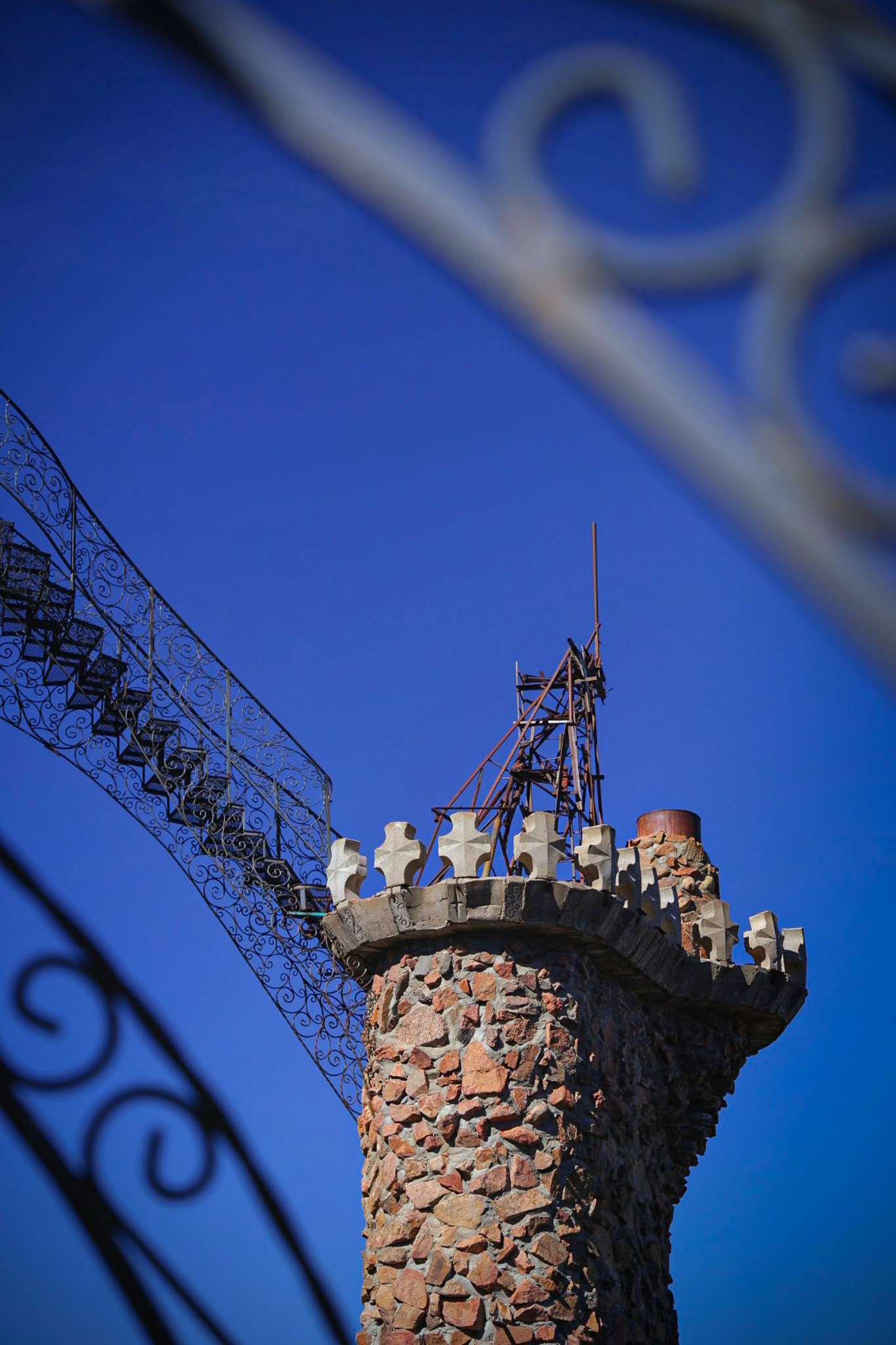Stone column and ornate wrought-iron gate against a vivid blue sky