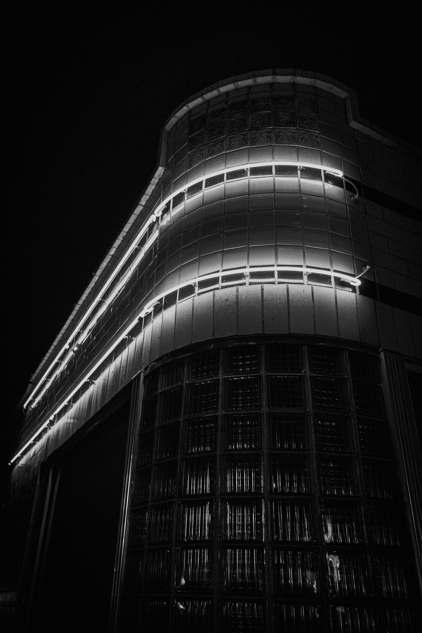Curved black building facade at night with horizontal neon light bands wrapping around glass block windows