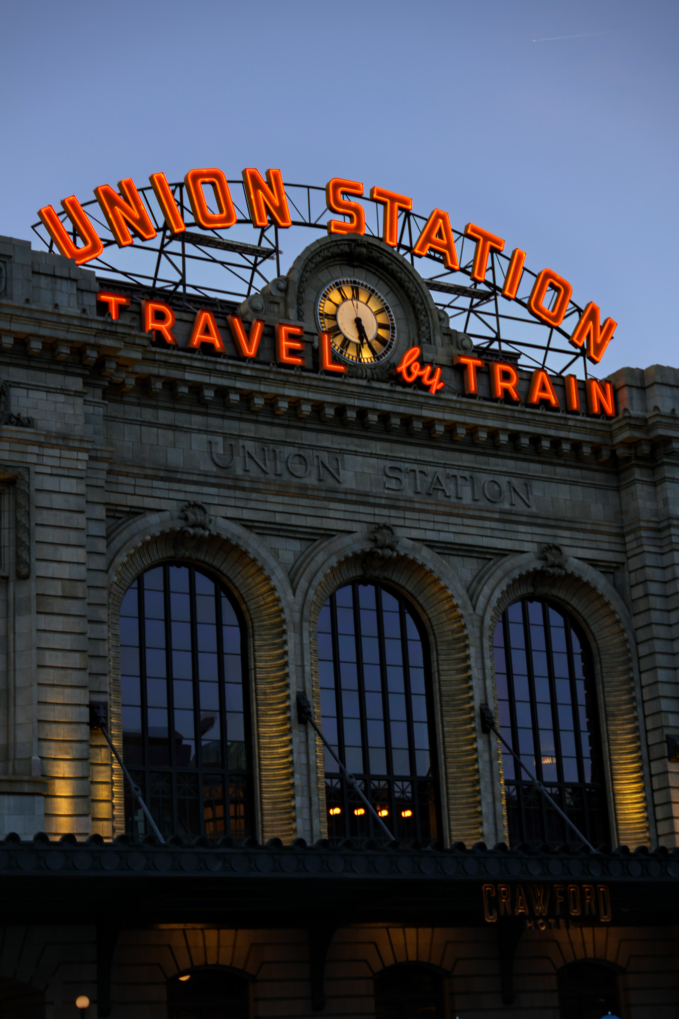 Denver Union Station with the neon Travel by Train sign at dusk