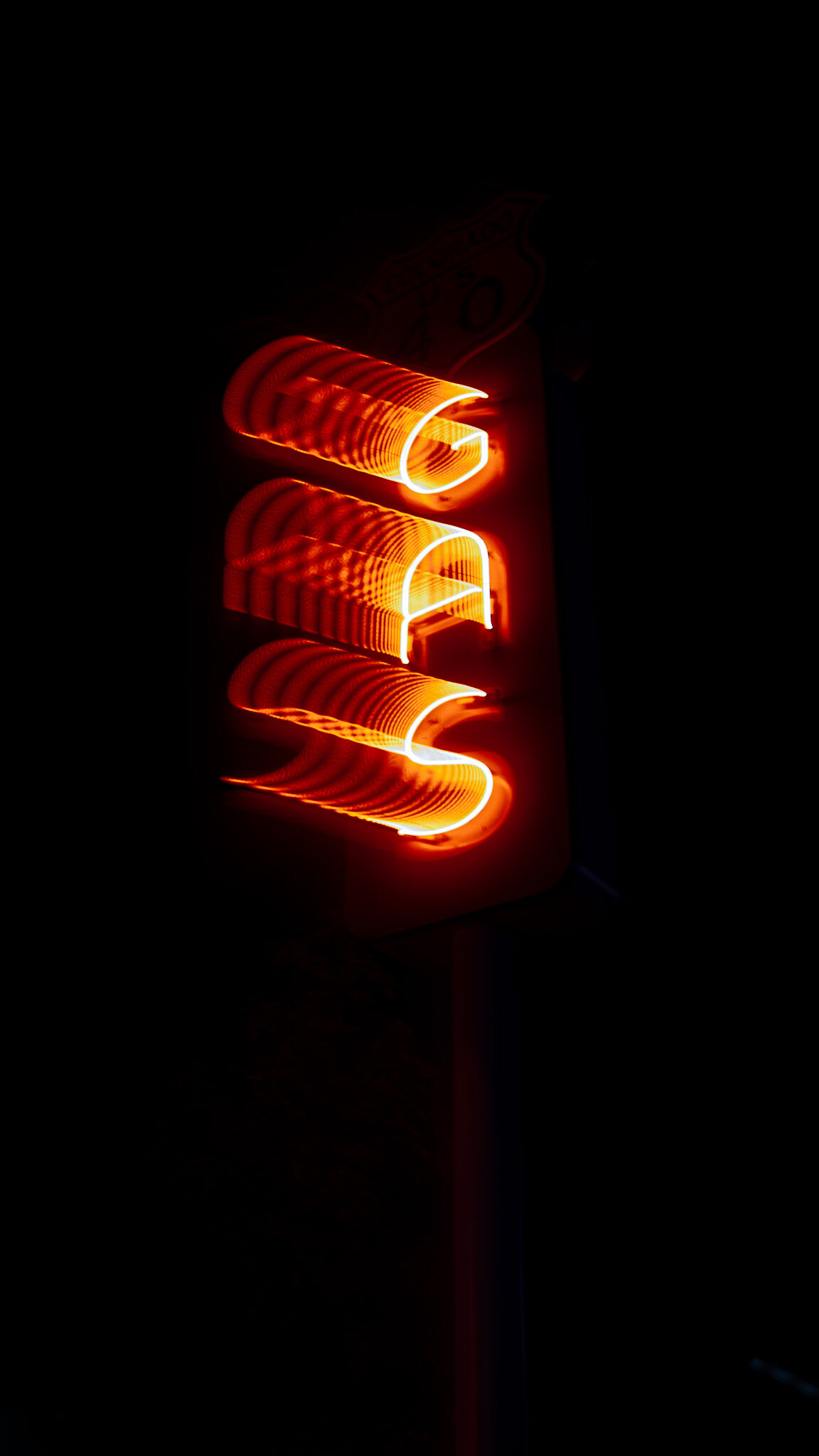 Close up of a vertical neon GAS sign glowing red and orange against pure black at night
