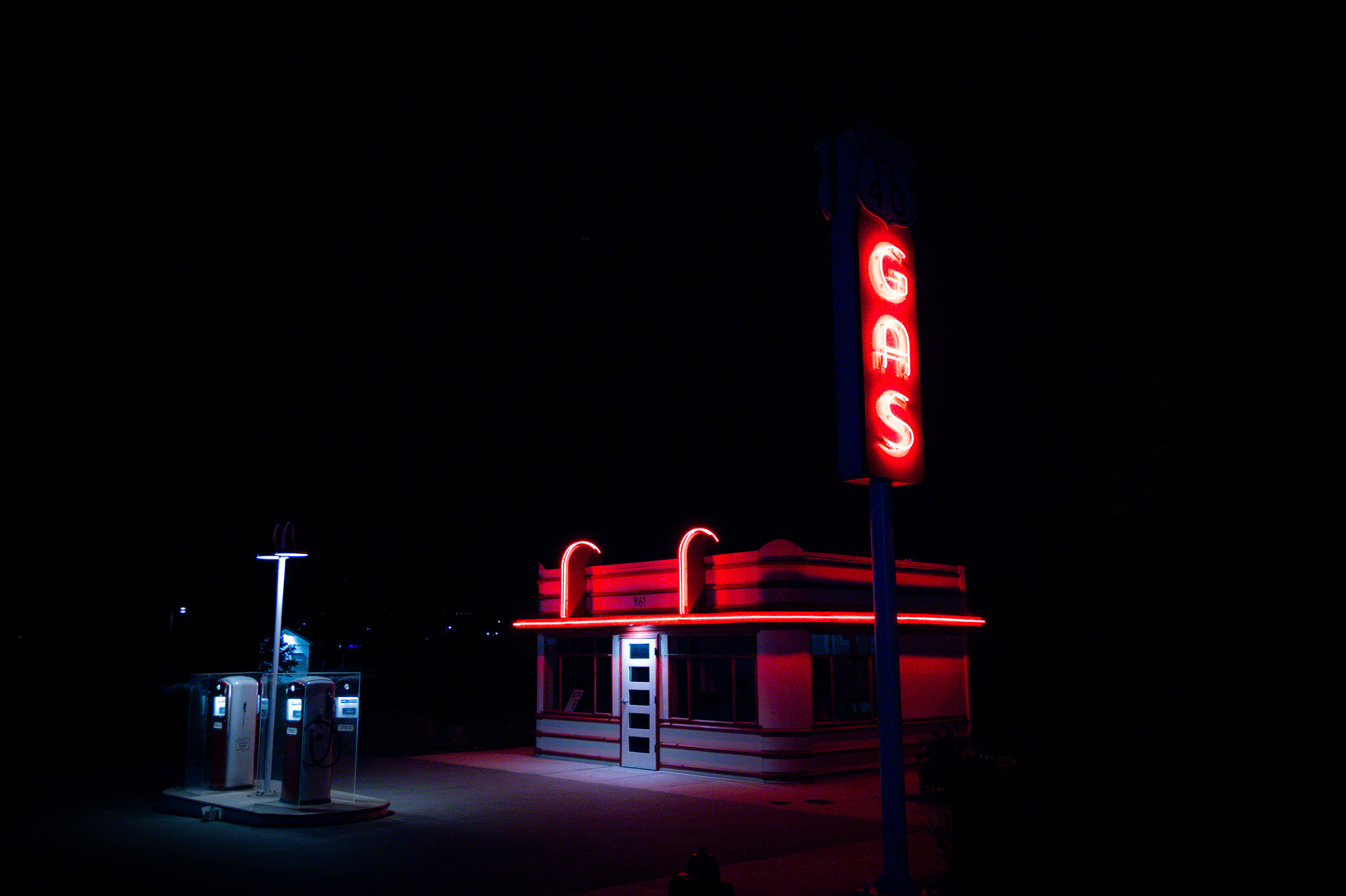 Roadside diner and gas pumps glowing red under a neon GAS sign at night