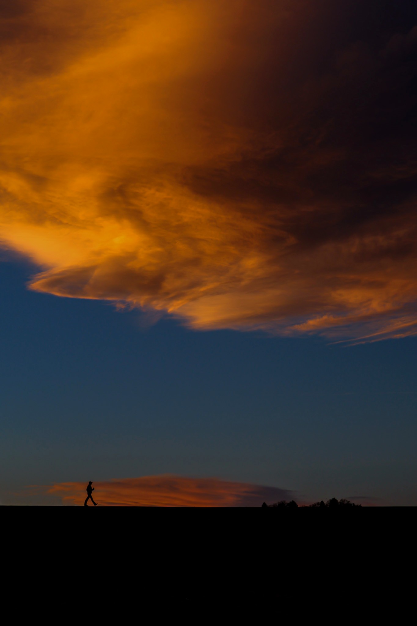 Lone figure walking, silhouetted against a vivid golden-hour sky