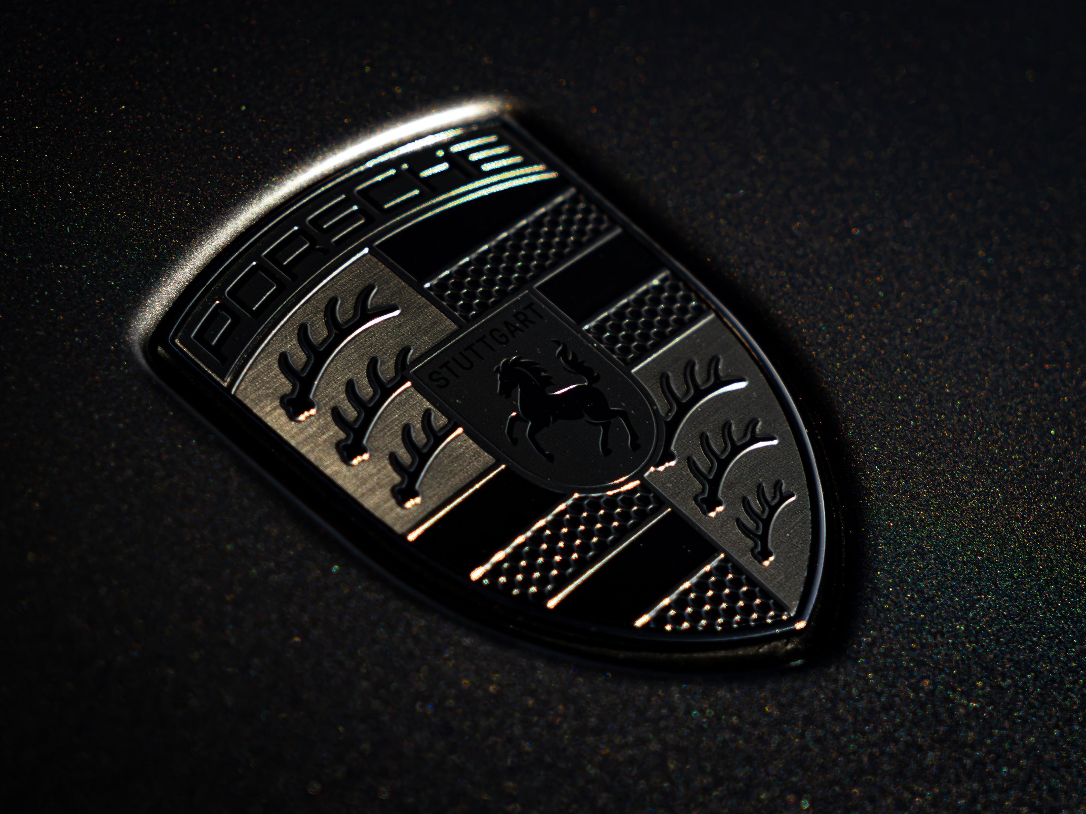 Macro shot of the gold Porsche crest badge on black sparkle paint, with a diagonal light streak