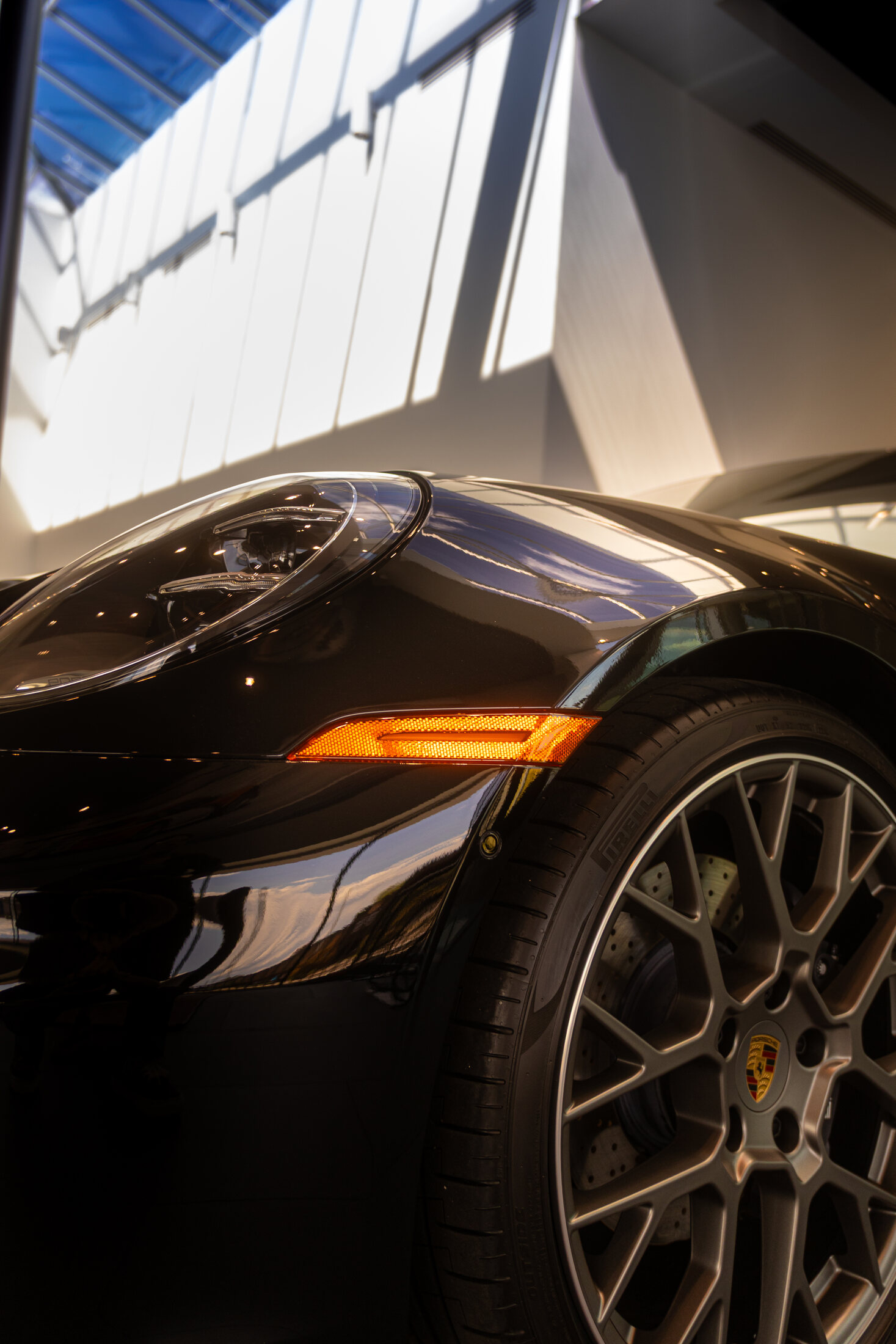 Close up of a black Porsche's wheel, orange indicator light, and skylight reflection along the fender