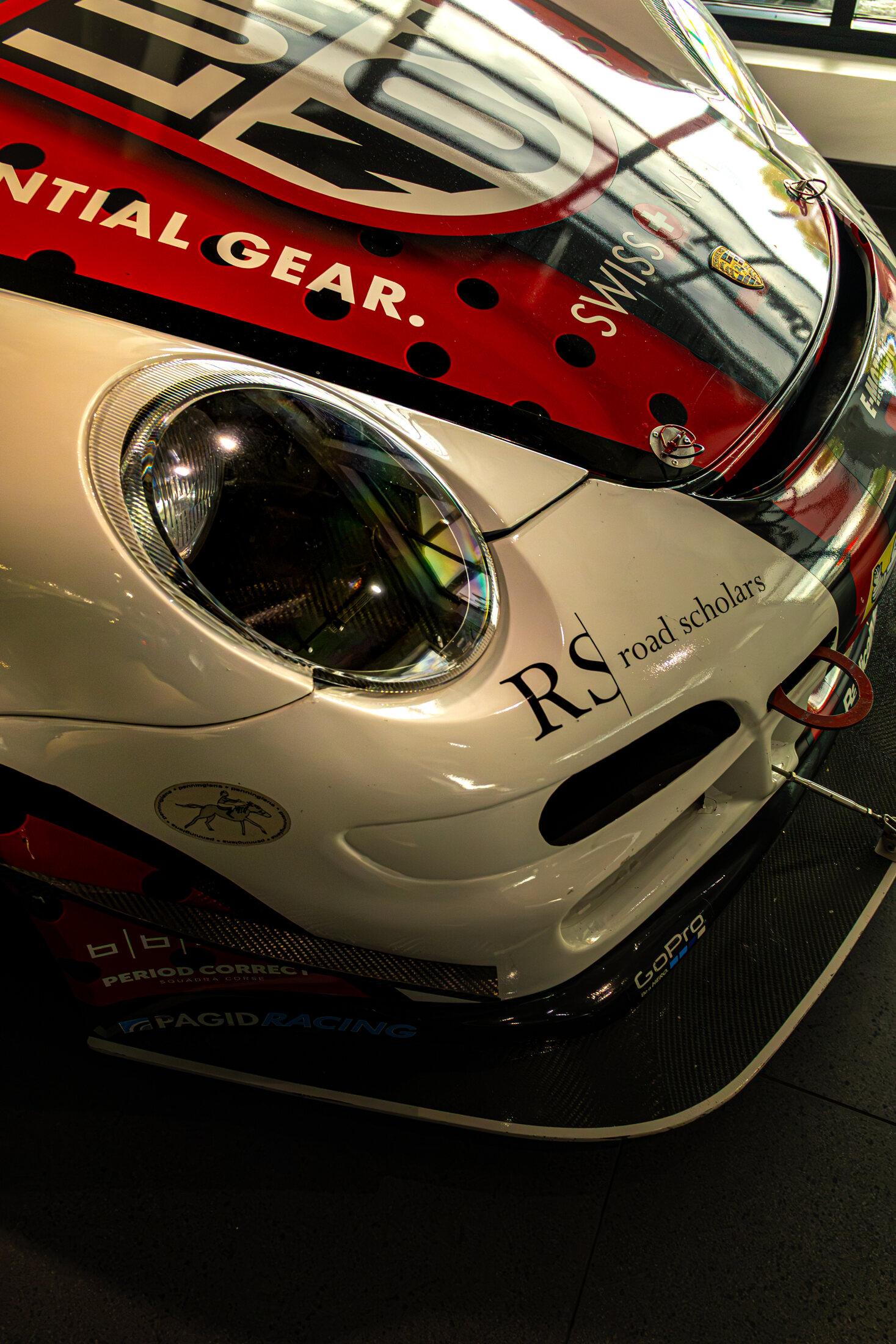 Extreme close up of a white Porsche GT3 Cup racecar's nose, headlight, and Road Scholars livery