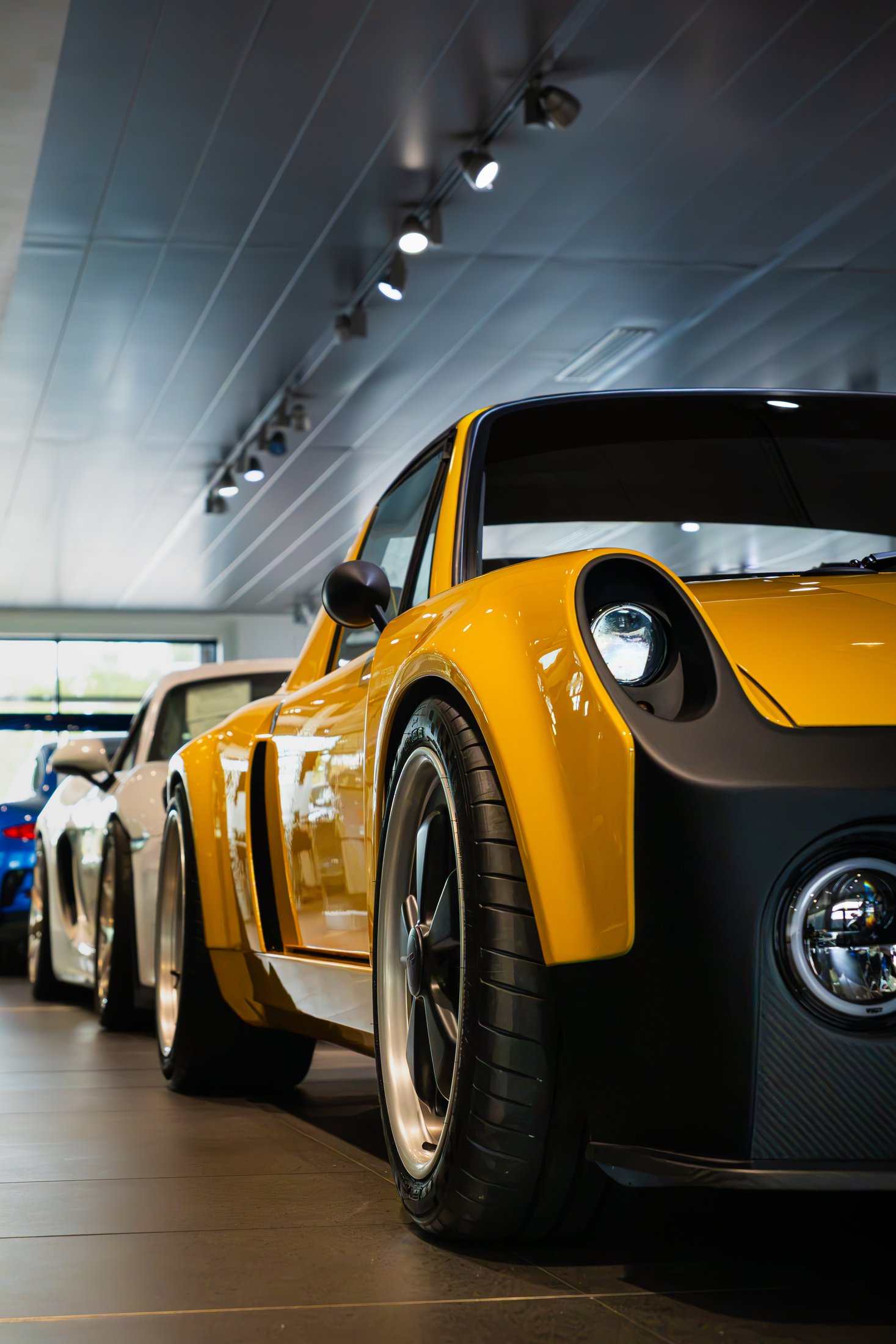 Yellow restomod Porsche with matte black fenders, seen low and close in a bright showroom